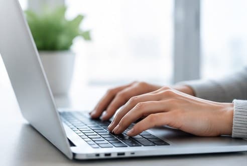 Close-up of hands typing on a laptop in a bright office